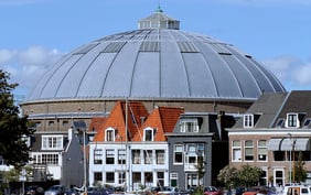 Traditional Dutch houses with orange-tiled roofs in front of the massive, silver-domed roof of the historic De Koepel monument in Haarlem, Netherlands. - Saviynt