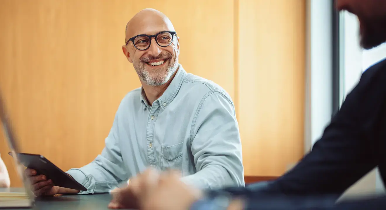 Smiling IT consultant discussing cyber risk management and enterprise identity solutions with a colleague on a tablet.