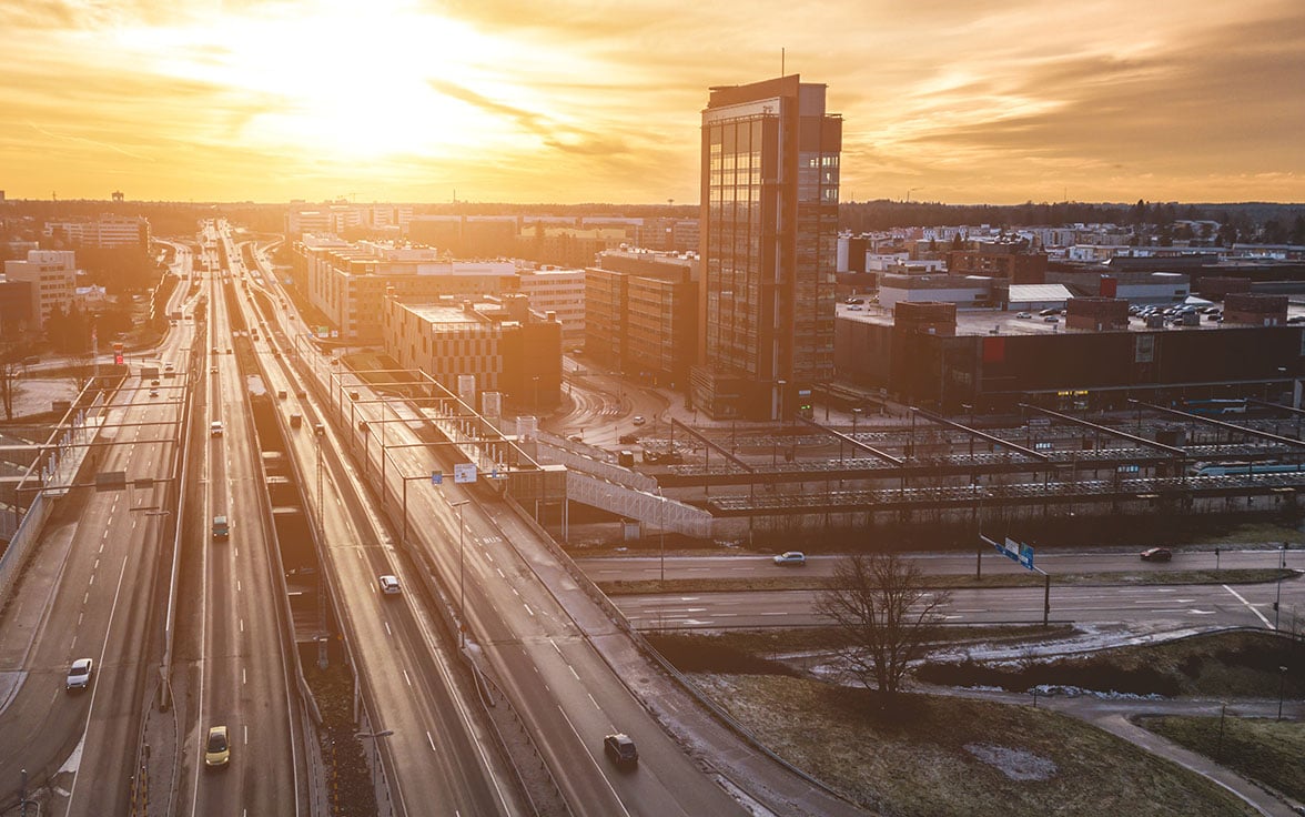 A high-angle view of the modern Espoo, Finland skyline and highway infrastructure captured during a bright golden sunset. - Saviynt