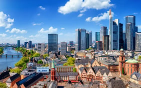 Striking high-angle view of Frankfurt showcasing the sharp contrast between the historic old town architecture in the foreground and the soaring modern skyscrapers of the financial district under a blue sky. - Saviynt