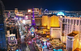 Vibrant aerial view of the Las Vegas Strip at night featuring the Paris Las Vegas Eiffel Tower replica, the Bellagio, Planet Hollywood, and the glowing Sphere against the city lights. - Saviynt