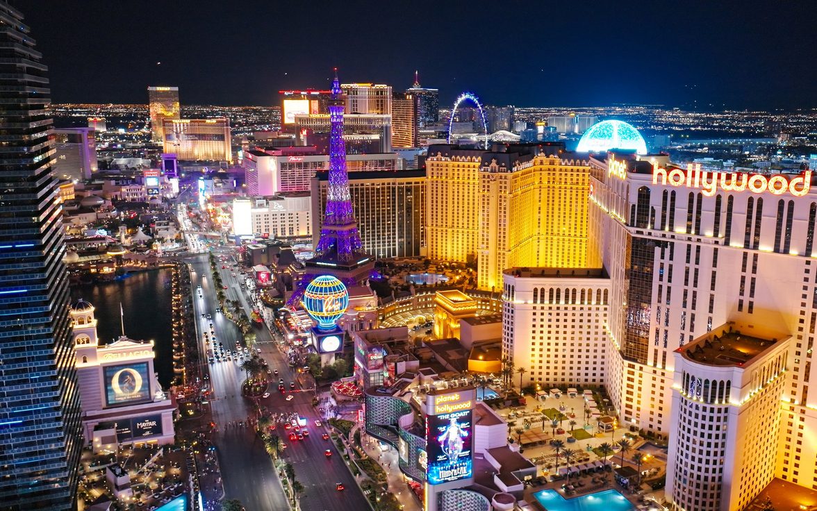 Vibrant aerial view of the Las Vegas Strip at night featuring the Paris Las Vegas Eiffel Tower replica, the Bellagio, Planet Hollywood, and the glowing Sphere against the city lights. - Saviynt