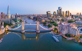 Stunning aerial twilight view of London showcasing the illuminated Tower Bridge over the River Thames, with The Shard and the city's financial district skyscrapers under a clear evening sky. - Saviynt