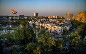 Aerial view of Connaught Place in New Delhi, India, featuring the Indian national flag in Central Park surrounded by circular architecture, lush trees, and city buildings under a clear sky.