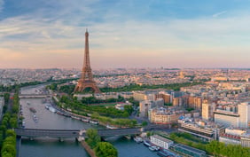 Beautiful aerial view of Paris showcasing the iconic Eiffel Tower standing tall next to the Seine River, with historic bridges and the sprawling cityscape bathed in a warm sunset glow. - Saviynt