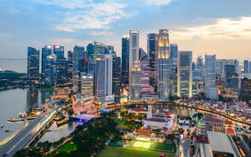 Aerial view of downtown Singapore's civic district and city skyline at dusk, featuring illuminated historic buildings, green lawns, and surrounding skyscrapers.