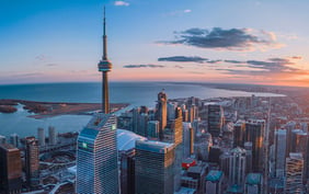 Gorgeous aerial view of the Toronto skyline at sunset, showcasing the iconic CN Tower standing tall above downtown skyscrapers and looking out toward Lake Ontario. - Saviynt