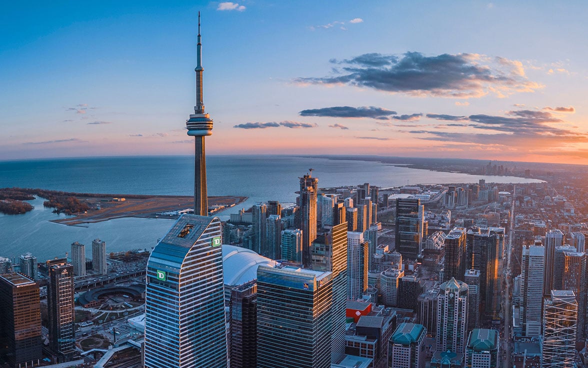 Gorgeous aerial view of the Toronto skyline at sunset, showcasing the iconic CN Tower standing tall above downtown skyscrapers and looking out toward Lake Ontario. - Saviynt