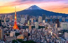Vibrant Tokyo city skyline at sunset featuring the illuminated Tokyo Tower in the foreground and a snow-capped Mount Fuji rising in the background under a colorful sky. - Saviynt